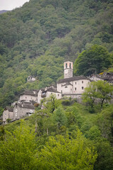 Old mid-century town full of stone houses, a church and a yellow car on a forest covered mountain side view from the bottom, Corippo, Switzerland