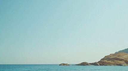 Fototapeta premium Calm sea meeting rocky coast under clear sky.
