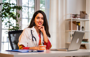 Young Indian dentist in white coat explaining oral health via video call with a model denture