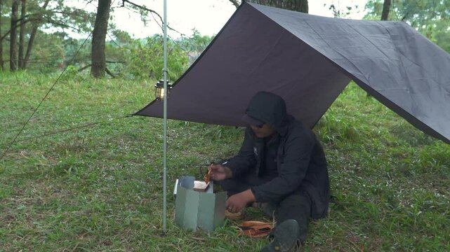 The concept of Bushcraft camping alone in a pine forest area while cooking curry with roti canai. An Asian male adventurer is solo camping while preparing and cooking in beautiful nature