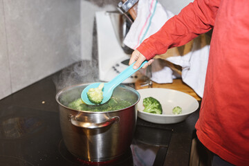 Child scooping broccoli from a steaming pot on the stove.