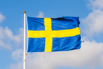 The national flag of Sweden flying in the wind at full mast against blue sky with white clouds.