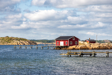 Seascape on the Resö island in the Bohuslän province, Sweden, showing a typical red painted boathouse on the rocky coast with a wooden pier under a stormy sky on a sunny summer day.