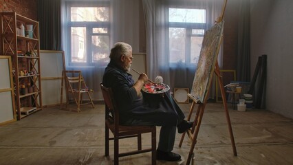 Elder man spending his free time with hobby, visiting art studio class, sitting painting picture...