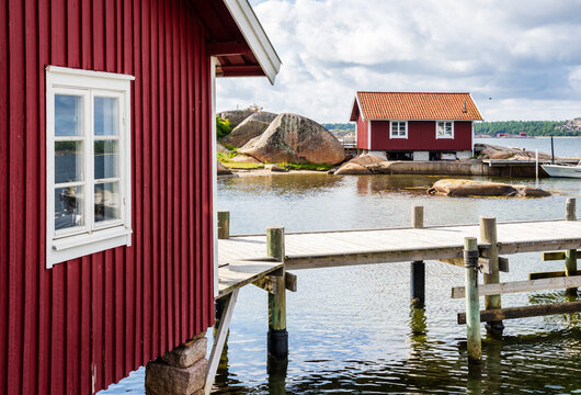 Two red painted boathouses with tiled roofs and a wooden pier on the pink granite coast in the Bohusl&auml;n province, Sweden, under a stormy sky on a sunny summer day.