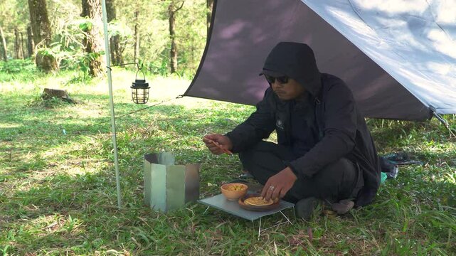 The concept of Bushcraft camping alone in a pine forest area while cooking curry with roti canai. An Asian male adventurer is solo camping while preparing and cooking in beautiful nature