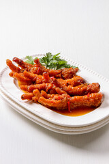 A plate of Chinese style spicy braised chicken feet in a sweet and spicy sauce garnished with fresh parsley in isolated white background