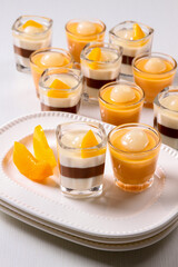 A group of elegant dessert cups with layers of creamy pudding, chocolate mousse and topped with fresh sliced orange & lychee in isolated white background