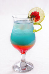 Colorful layered cocktail with blue, green, orange, and red hues garnished with a lime wedge and strawberry in isolated white background