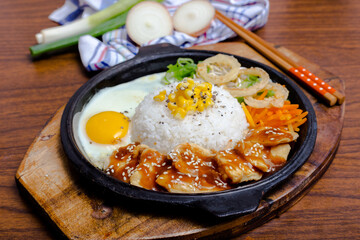 Yakiniku chicken served with steamed white rice, a sunny-side-up egg and crispy onion rings on a hot plate
