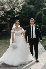 couple on a wedding walk. A woman is dressed in a white off-the-shoulder wedding dress and holds a bouquet of white flowers in her hands.