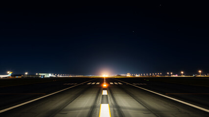 An illuminated airport runway at night, with glowing guide lights leading to the horizon under a starry sky