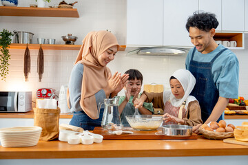 Asian muslim father, mother and brother cheer up the girl to mix flour in the bowl and stay together in kitchen of their house.