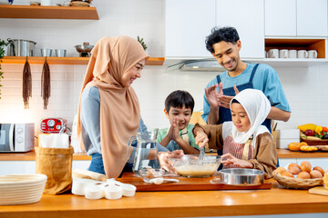 Asian muslim father, mother and brother cheer up the girl to mix flour in the bowl and stay...