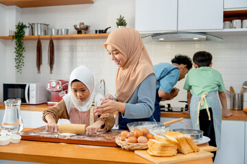 Wide shot of little Asian muslim girl enjoy to use rolling pin to make some bakery and support...