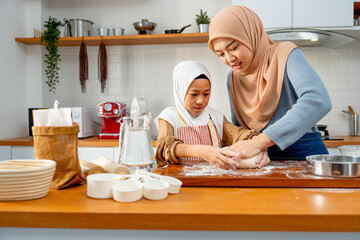 Young Asian muslim mother help and teach her daughter to threshing flour by hands on wooden tray...