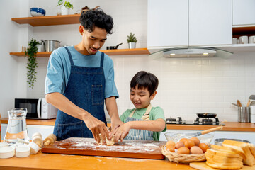 Front view of Asian father stand beside his son during teaching the boy to threshing flour for making bakery in kitchen of their house.
