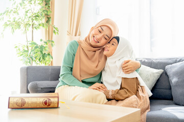 Asian muslim mother sit on sofa beside of her daughter and hug her child they also smiling in concept of happiness muslim family at home.