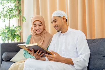 Couple muslim man and woman sit on sofa and read islam teaching book together and they smile with happiness.