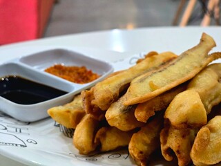 A plate of golden fried banana fritters served with dipping sauces. The dish highlights a popular snack or dessert, showcasing crispy batter and sweet flavors, ideal for promoting traditional cuisine 