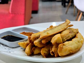 A plate of golden fried banana fritters served with dipping sauces. The dish highlights a popular snack or dessert, showcasing crispy batter and sweet flavors, ideal for promoting traditional cuisine 
