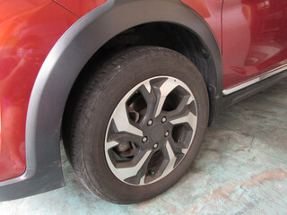 One of The Used and Worn Dirty Black Rubber Car Tire On The Light Blue Cement Garage Floor. Famous Branded Japanese Car. Red Car Paint. Beautiful Shot Close Up and Low Key Photography Image. JPG