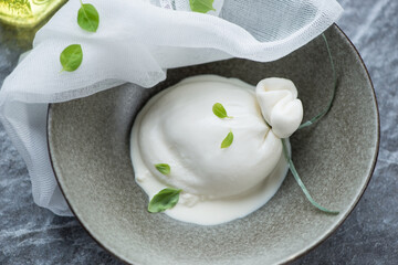 Olive-colored bowl with freshly made burrata cheese and green basil, middle close-up, horizontal shot
