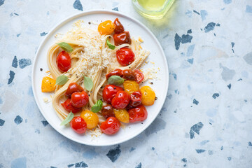 Plate with roasted cherry tomatoes and linguine, flat lay on a blue and white granite background, horizontal shot with space