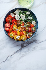 Bowl of cherry tomatoes, green beans and blue cheese salad, above view on a white stone background, vertical shot with space