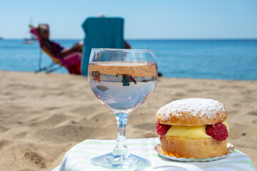 Lunch on sandy beach in Saint-Tropez with cake Tarte tropezienne filled brioche with cream and fresh red berries and glass of rose wine, summer vacation on French riviera, France