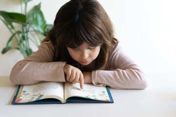 Little child girl reading a book at home.
