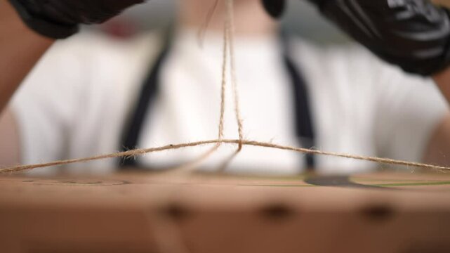 Closeup of gloved hands tying string around a package, showcasing precision in essential packaging tasks
