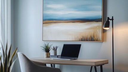 A desk with a laptop and a framed painting of a beach