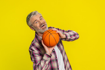 Mature man skillfully bounces basketball on hands, play game, showcasing confident flair, smooth control. Middle-aged guy on yellow background demonstrates athletic finesse, twirling ball on fingertip