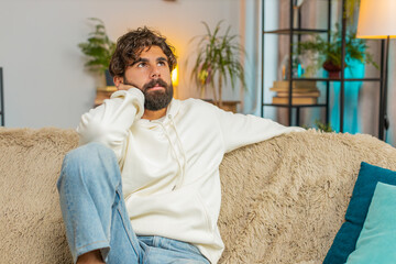Sad lonely man sits at home room looks pensive thinks over life concerns or unrequited love suffers...
