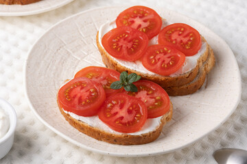 Delicious open-faced sandwiches topped with fresh tomatoes and cream cheese served on a textured white plate