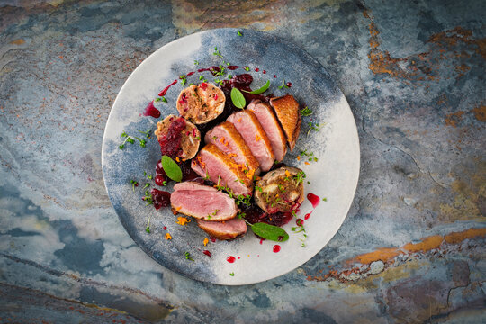 Roasted duck breast filet with homemade bread mushroom dumplings, orange topping and herbs served with cranberry sauce as top view on a design plate