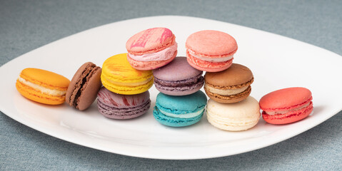 Close up delicious macaroon cookies in fresh mint green vanilla beige chocolate brown orange and pink colors. Light grey background, white plate. Contrast bright combination, bakery culinary.