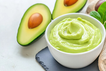Fresh guacamole dip with avocado halves on white table