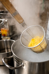 A close-up of fresh pasta being lifted from a pot of boiling water with a slotted spoon. Steam rises, creating a warm and inviting atmosphere in the kitchen. Perfect for culinary themes.