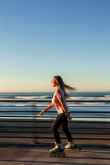vertical Young woman roller skating by the beach at sunset enjoying the ocean view © EDER