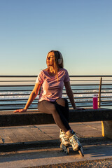 Sportswoman relaxing on bench wearing inline skates and listening music at sunset