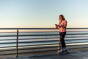 Sportswoman using mobile phone and wearing inline skates at sunset by the sea copyspace