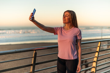 Sportswoman taking selfie with smartphone after inline skating training at sunset on the beach