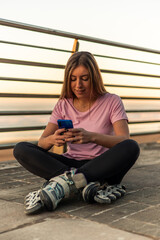 Young woman wearing inline skates using mobile phone at sunset