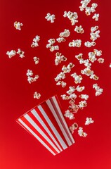 Fototapeta premium Close-up of popcorn spilling out from an old-fashioned red and white striped cinema bucket, against a vibrant red background