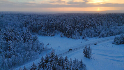 The car is driving along the road in a snow-covered white spruce forest at sunset