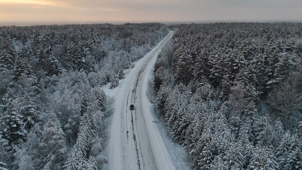 The car is driving along the road in a snow-covered white spruce forest at sunset