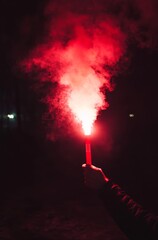 A hand holding a red flare, with smoke in the dark sky