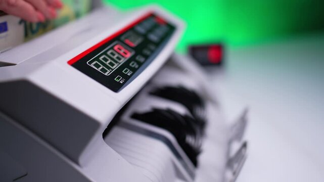 Money counting machine with rotating blades. Hand moves the bills and device quickly counts cash. Close up. Blurred backdrop.